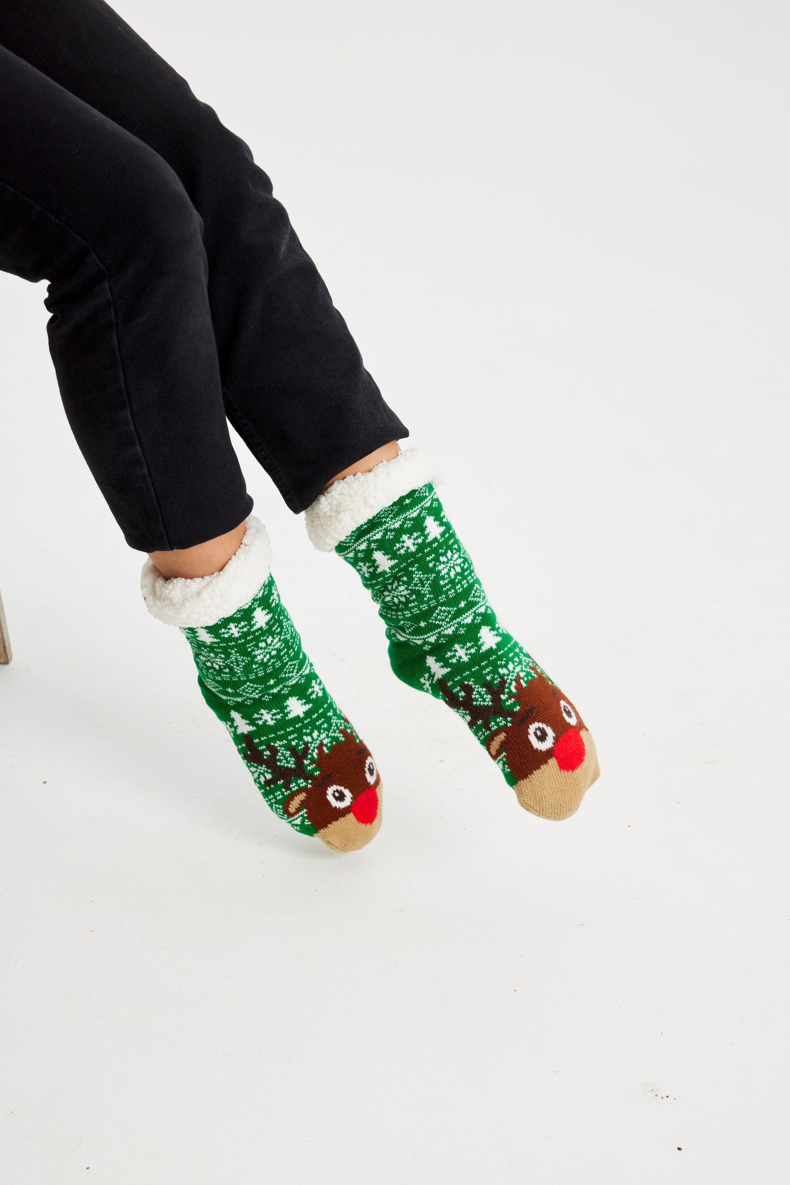 Ein Paar Beine, die ein Paar grüne Weihnachtssocken mit einem Rentier darauf tragen.